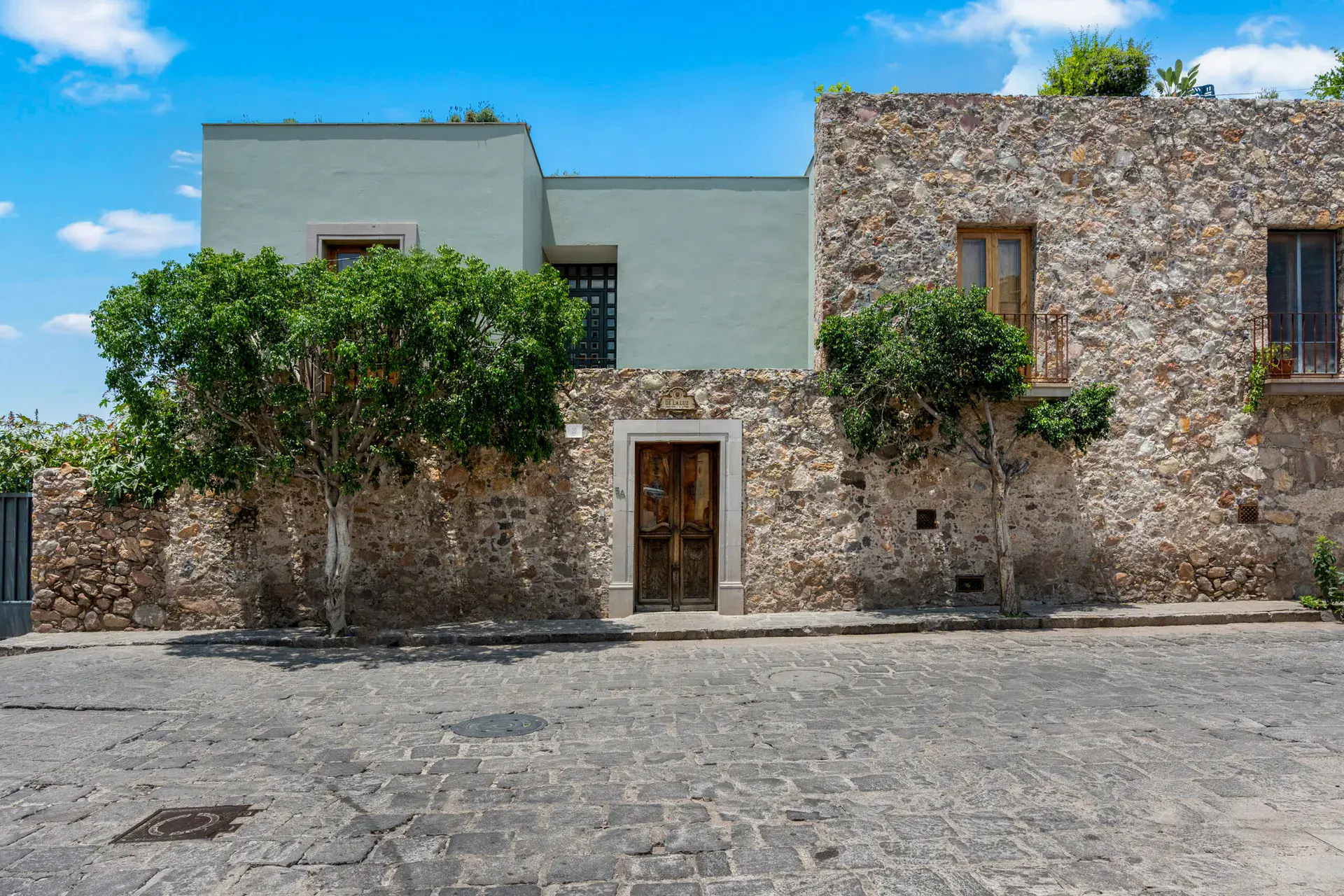 Casa Lula, stone and sage-green facade with trees on a cobblestone street, San Miguel de Allende