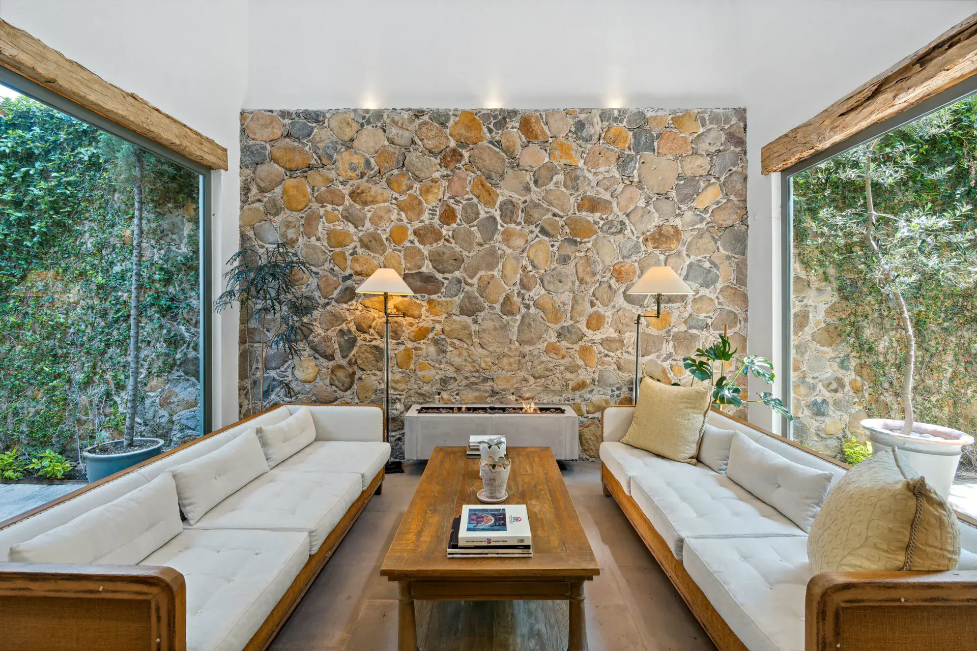 Casa Lula, living room with white sofas and a stone wall between tall windows, San Miguel de Allende