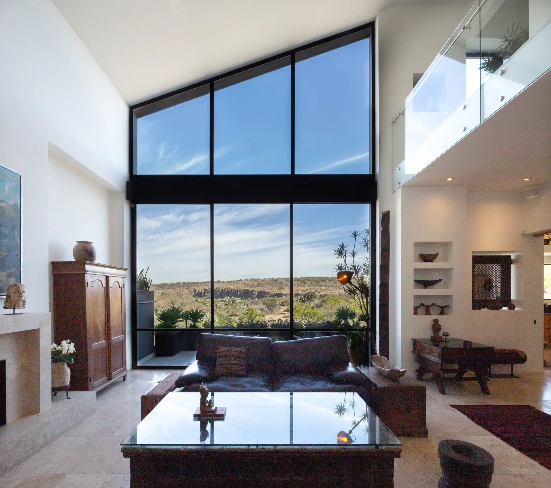 Casa Luz, double-height living room with floor-to-ceiling windows overlooking the valley and a glass-railed mezzanine, San Miguel de Allende