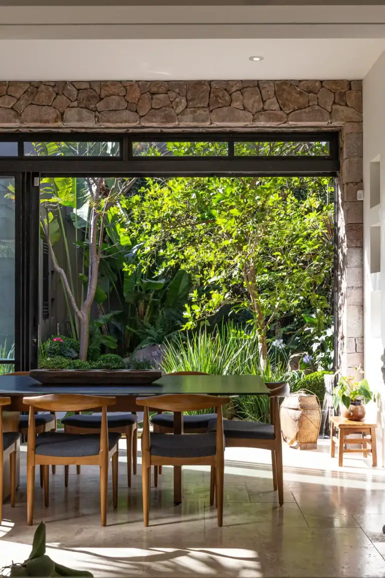 Casa Luz, dining table with wooden chairs beside a glass wall opening to a tropical garden, San Miguel de Allende