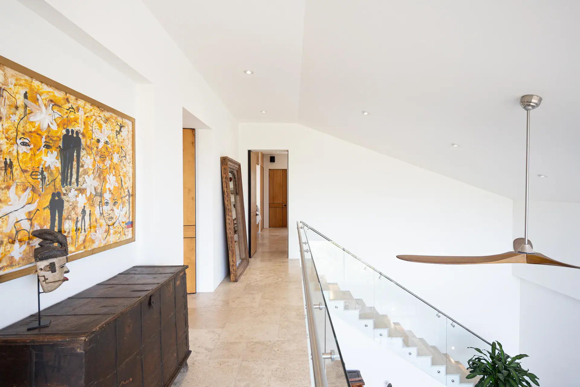 Casa Luz, upstairs hallway with a large yellow painting, carved chest and a glass-railed staircase, San Miguel de Allende