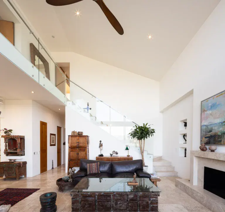 Casa Luz, living room with a glass coffee table below a mezzanine, staircase and fireplace, San Miguel de Allende