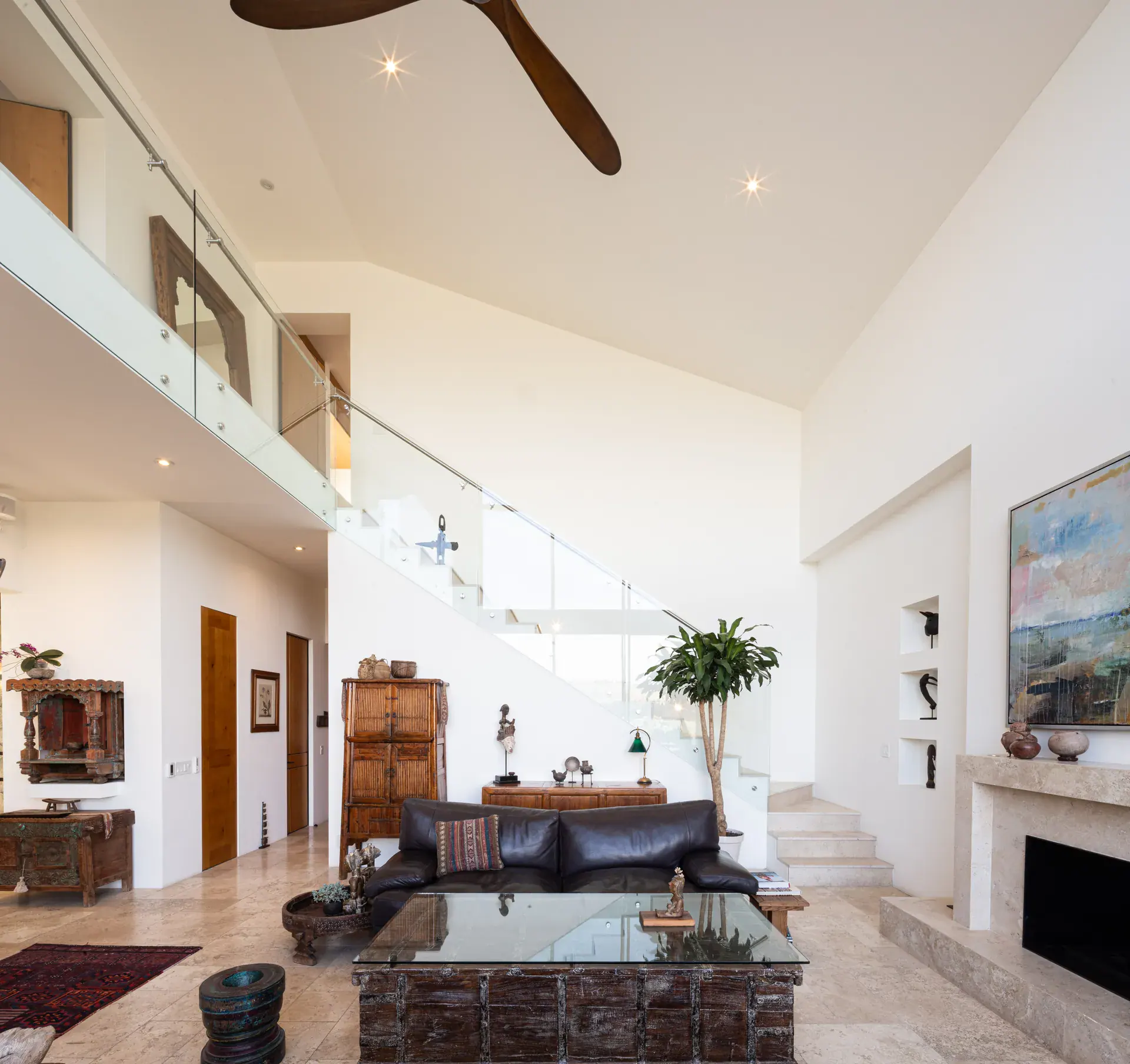 Casa Luz, living room with a glass coffee table below a mezzanine, staircase and fireplace, San Miguel de Allende