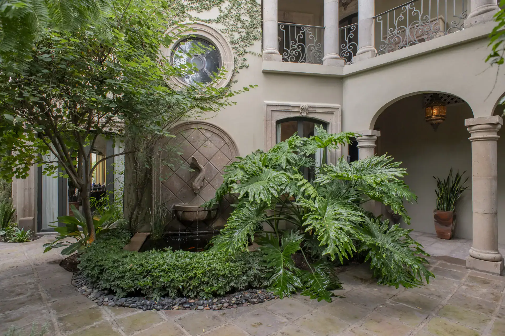 Casa Lyla, courtyard with an arched loggia, a wall fountain, a balcony above and tropical plants, San Miguel de Allende