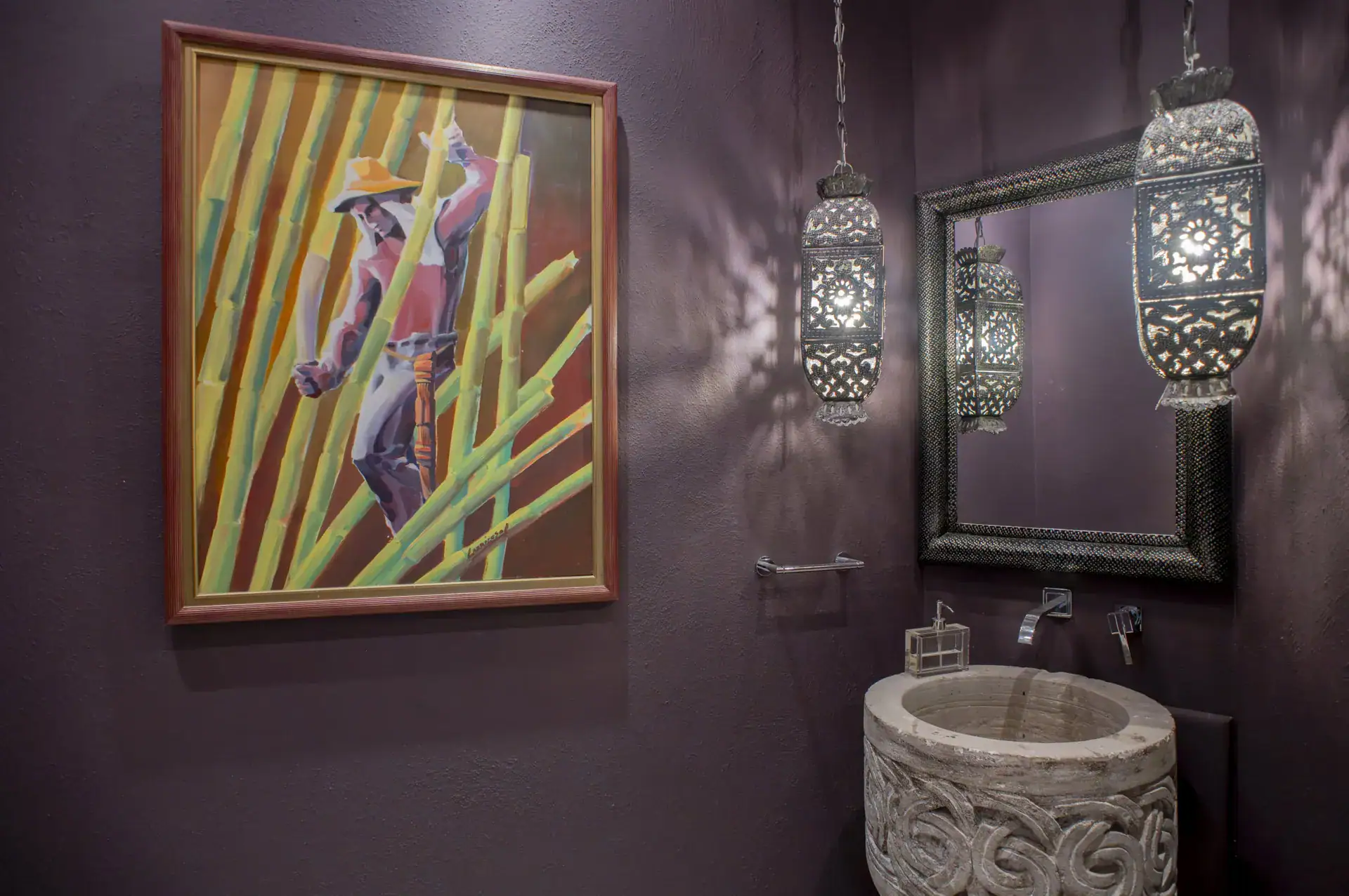 Casa Lyla, powder room with a purple wall, a colorful painting, a carved stone sink and Moroccan lanterns, San Miguel de Allende