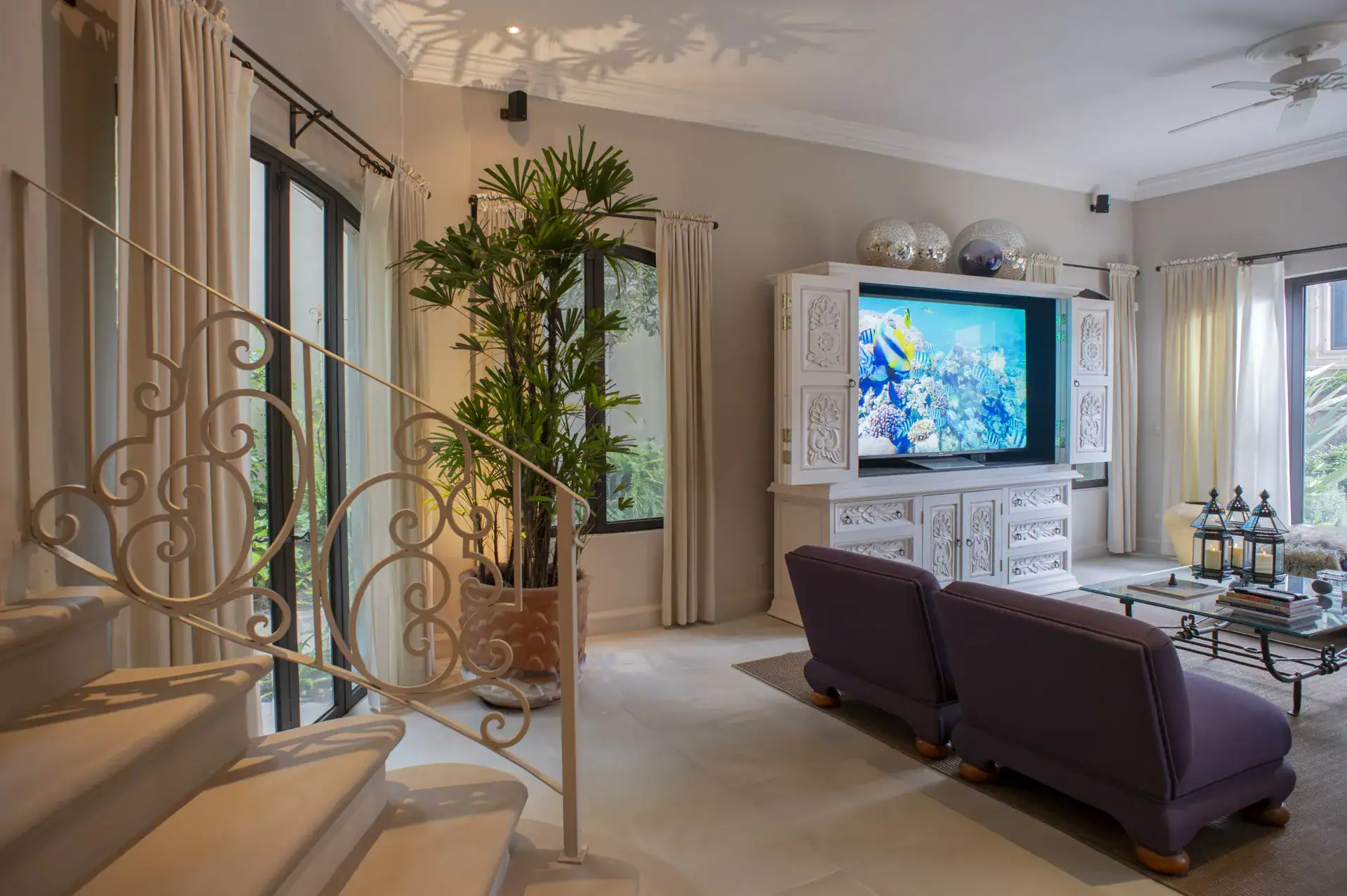 Casa Lyla, family room with purple armchairs, a wall television cabinet and a curved wrought-iron staircase, San Miguel de Allende