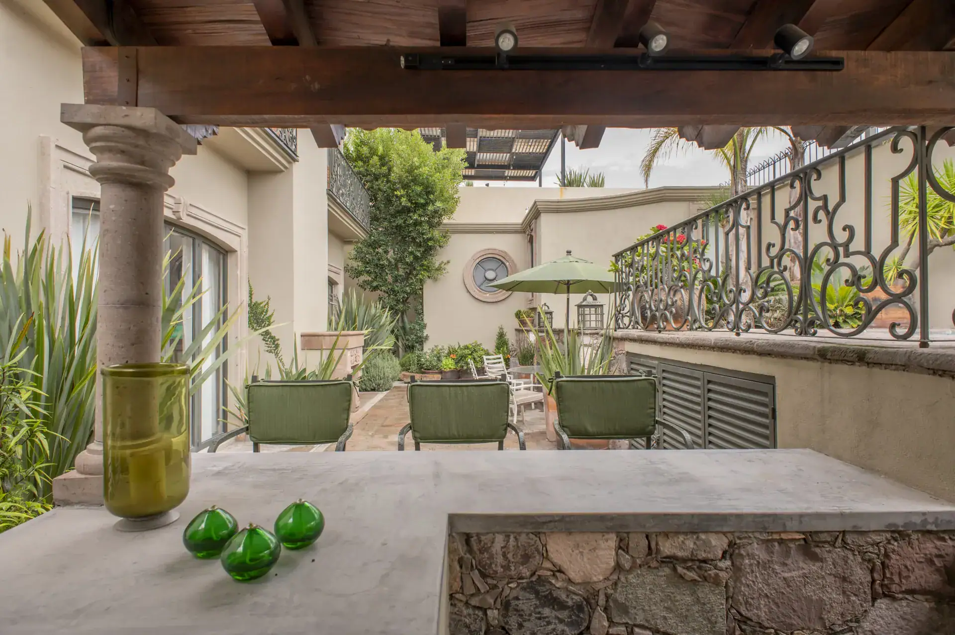 Casa Lyla, covered terrace with a stone column, a built-in counter and green chairs overlooking the patio, San Miguel de Allende