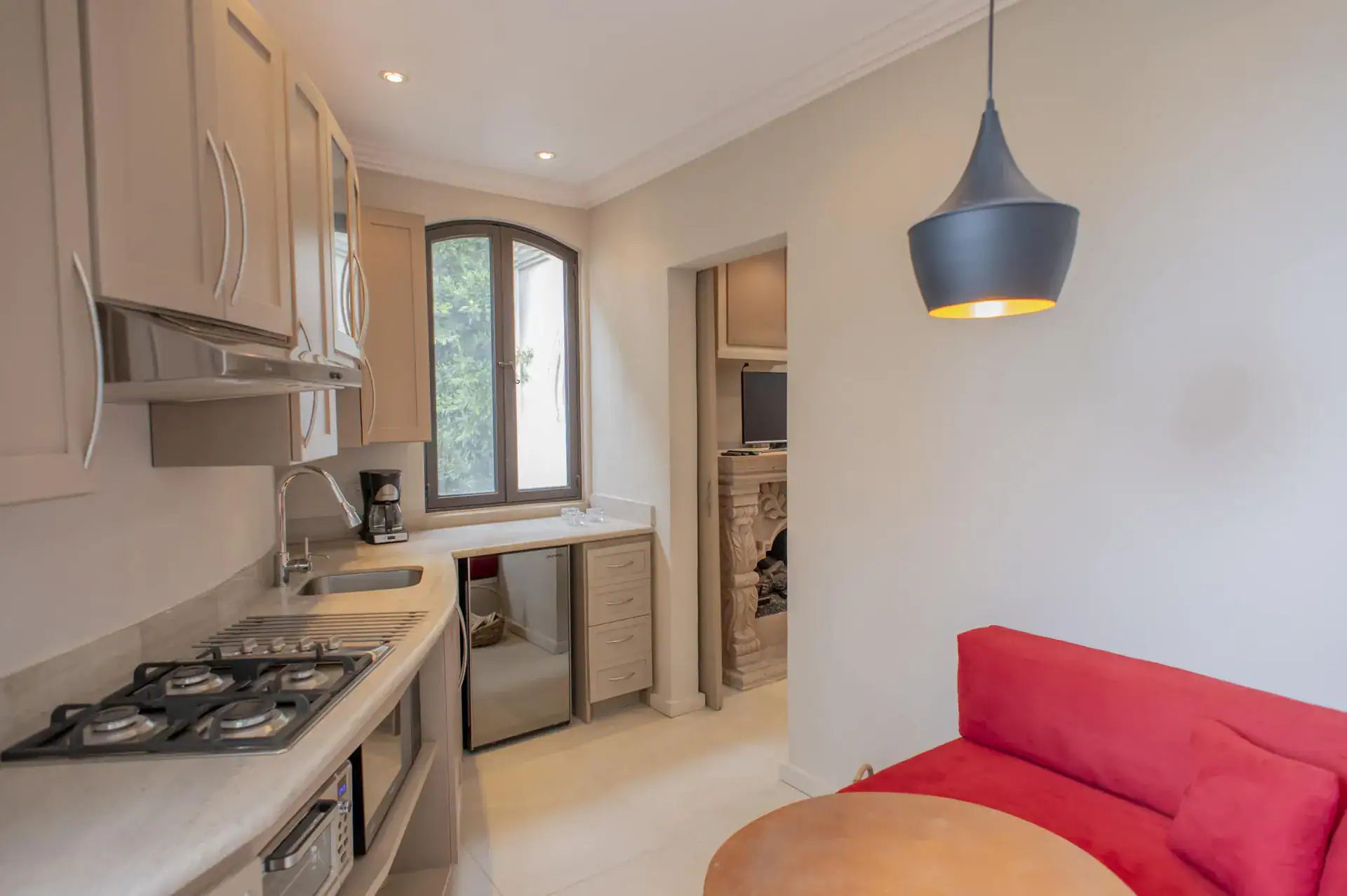 Casa Lyla, casita kitchenette with a red sofa, a gas cooktop and a black pendant light, San Miguel de Allende