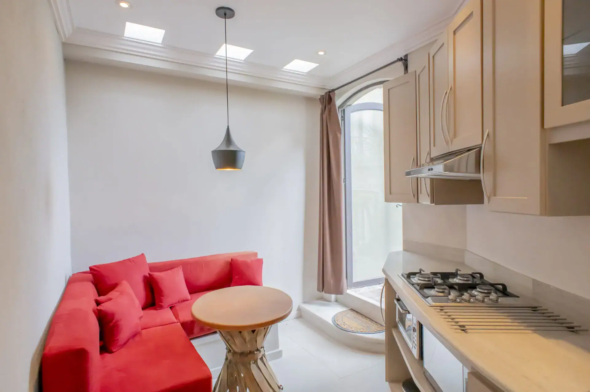 Casa Lyla, casita sitting area with a red sectional sofa, a pendant light and a tall window, San Miguel de Allende
