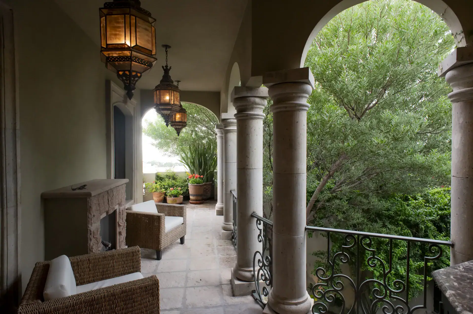 Casa Lyla, loggia with stone columns, lanterns and wicker chairs overlooking the trees, San Miguel de Allende