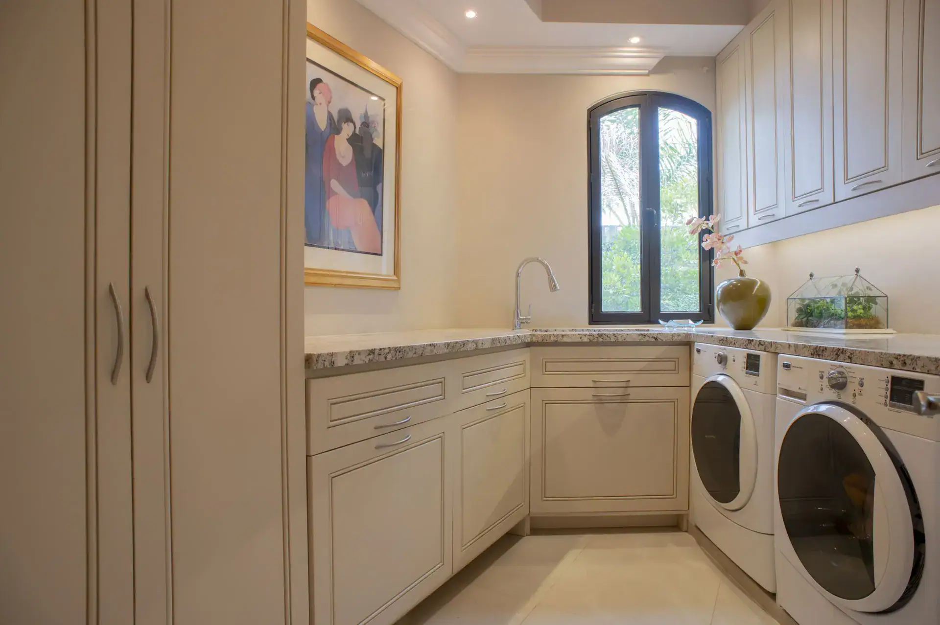 Casa Lyla, laundry room with a washer and dryer, beige cabinets and an arched window, San Miguel de Allende