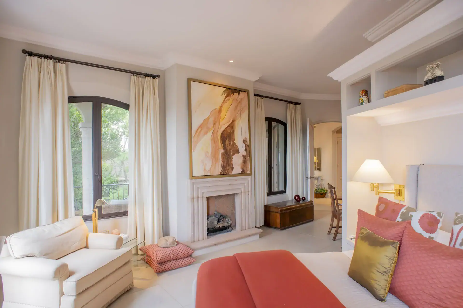 Casa Lyla, bedroom with a coral bed, a fireplace, a white armchair and tall windows, San Miguel de Allende