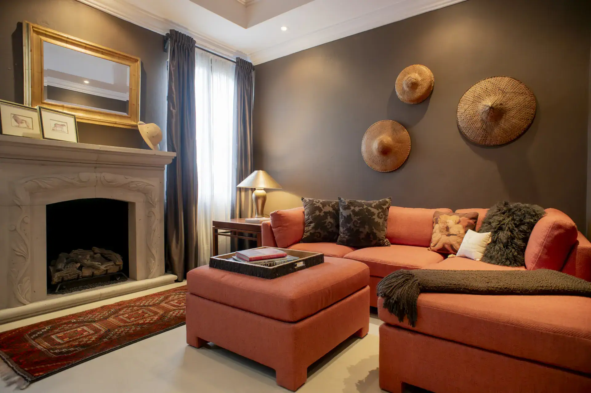 Casa Lyla, sitting room with an orange sectional, a stone fireplace and woven hats on the wall, San Miguel de Allende