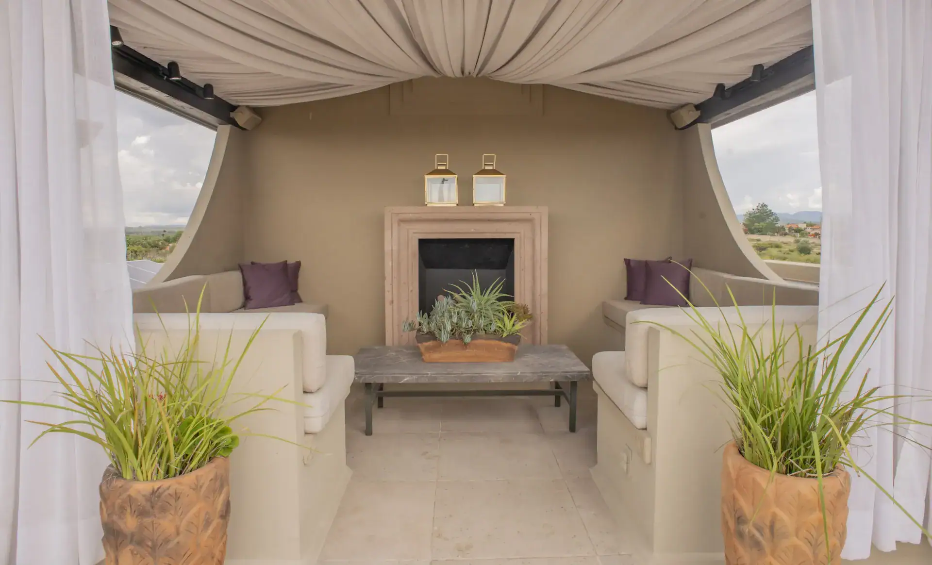Casa Lyla, covered rooftop lounge with curtains, two built-in sofas and a fireplace, San Miguel de Allende