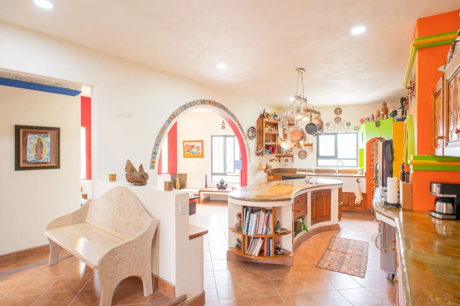 Casa Mexicana, open kitchen with a curved wood island with books, an arched pass-through and a bright mural wall, San Miguel de Allende