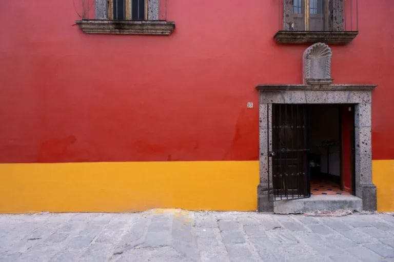 Casa Mexicana, red and yellow street facade with a stone-framed doorway and iron gate, San Miguel de Allende