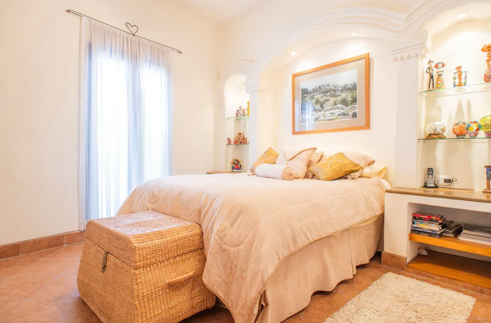 Casa Mexicana, bedroom with a cream bedspread, a wicker trunk, an arched headboard niche and sheer curtains, San Miguel de Allende