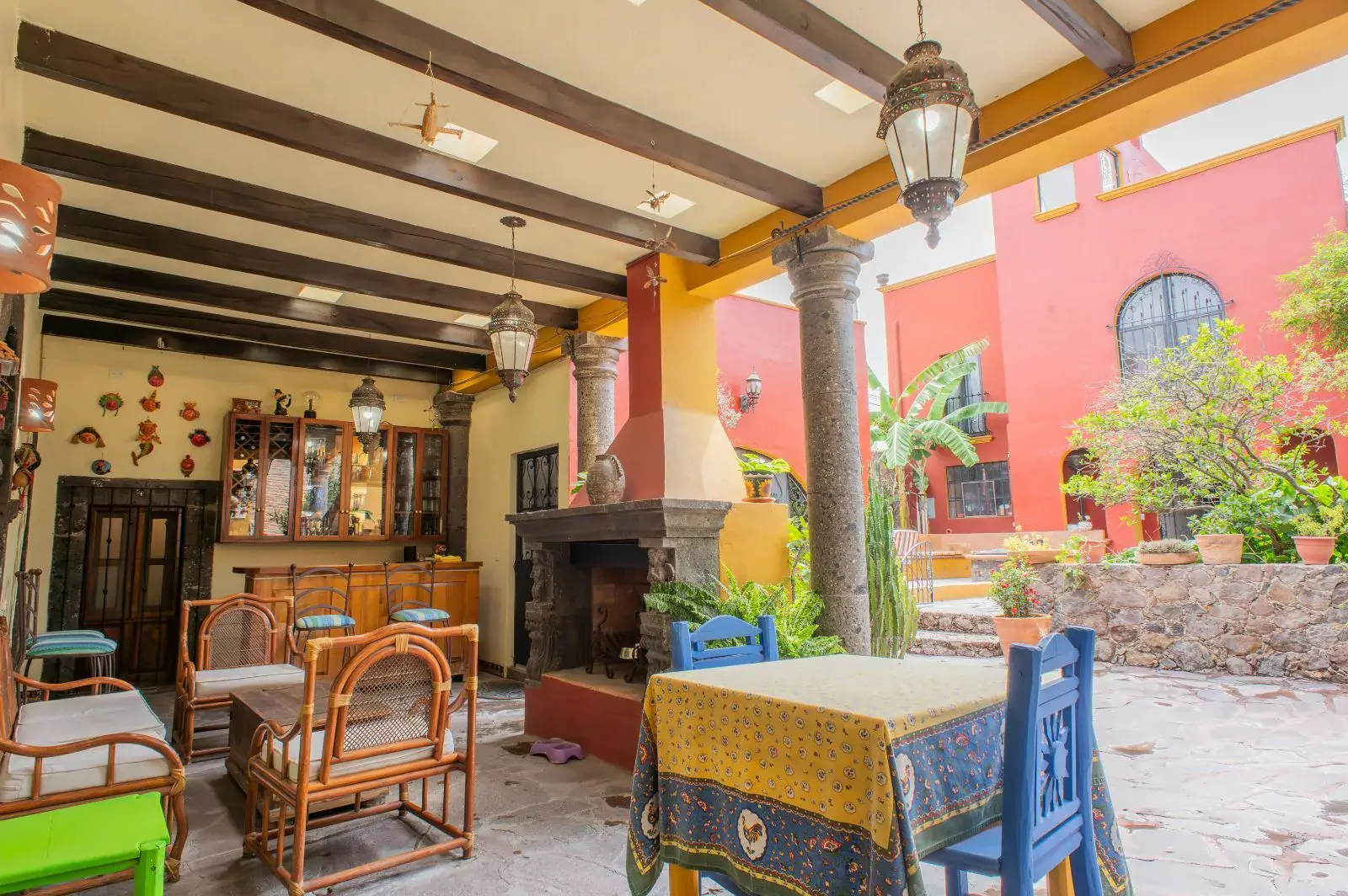 Casa Mexicana, covered patio with a stone column, a beamed roof, wicker chairs and a fireplace beside the courtyard, San Miguel de Allende