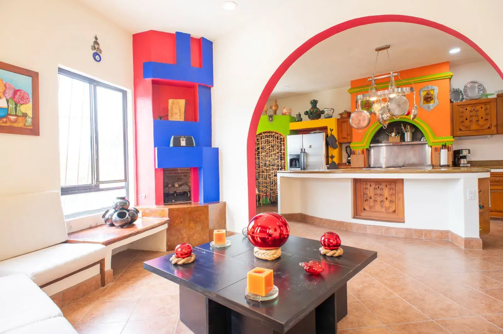 Casa Mexicana, living room with a blue and red tiled fireplace, a dark wood coffee table and a colorful open kitchen beyond, San Miguel de Allende