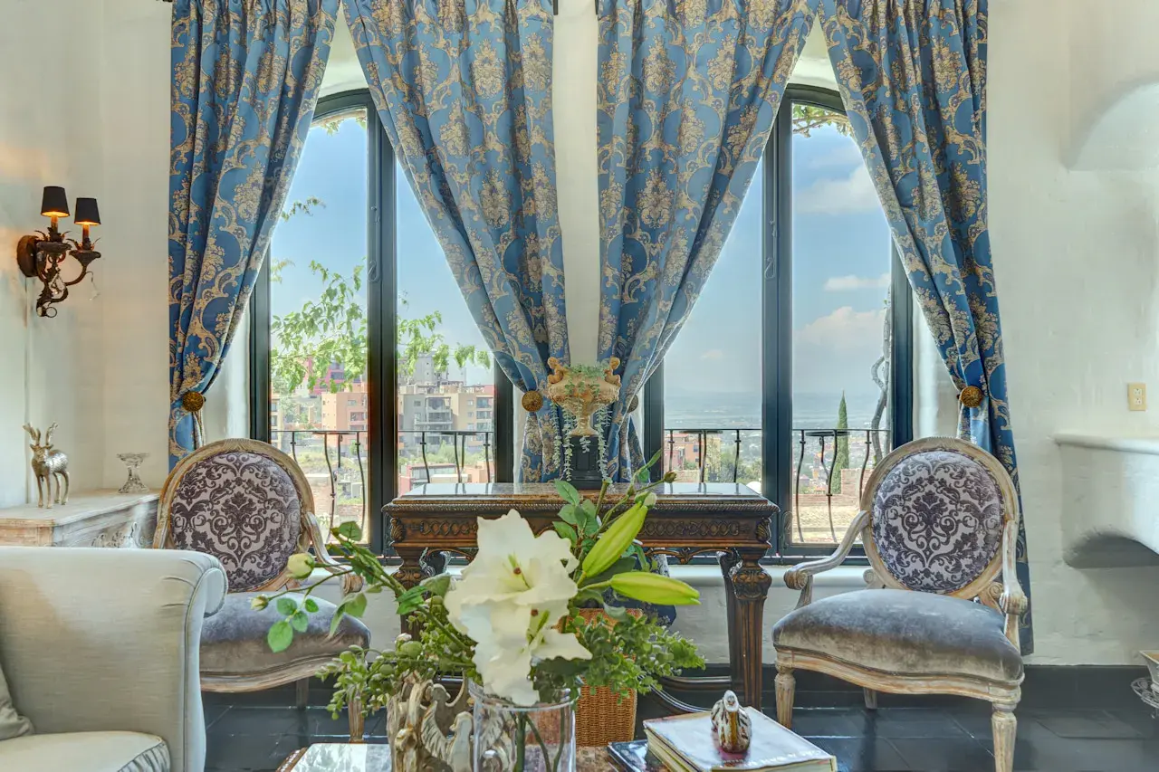 Casa Mi Besito, sitting area with blue and gold damask curtains, carved chairs and arched windows overlooking the valley, San Miguel de Allende