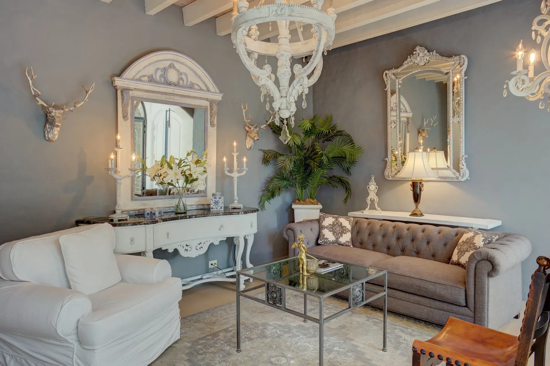 Casa Mi Besito, sitting room with antler mounts, ornate white mirrors, a gray tufted sofa and a glass coffee table, San Miguel de Allende