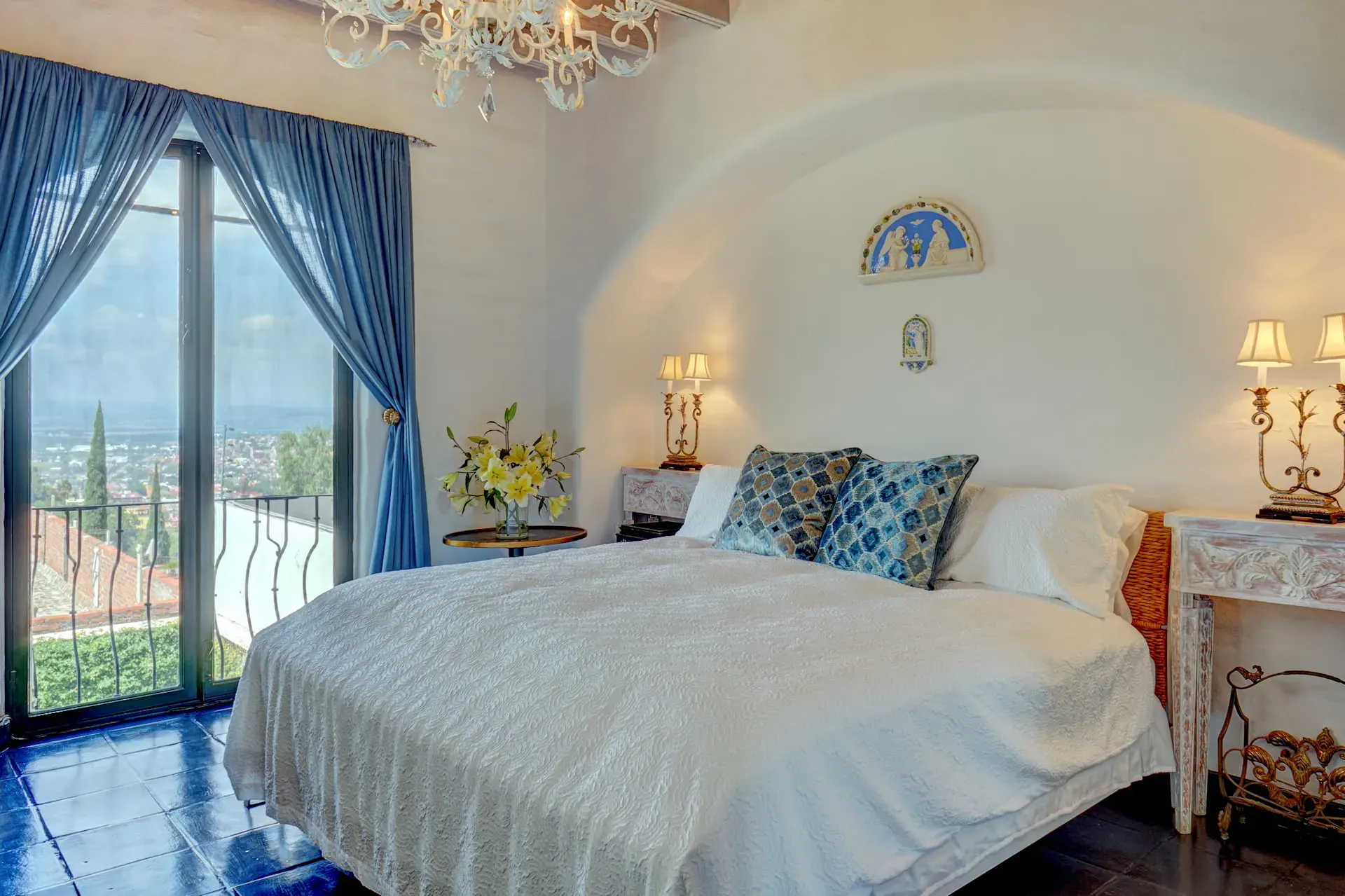 Casa Mi Besito, bedroom with a white bedspread, blue drapes and glass doors to a balcony with a valley view, San Miguel de Allende