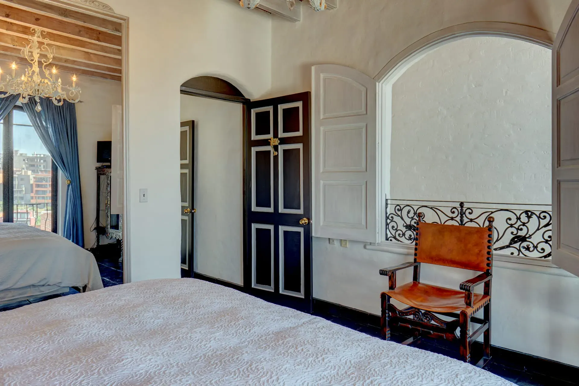 Casa Mi Besito, bedroom with a black and white door, an arched niche with a carved iron rail and a leather chair, San Miguel de Allende