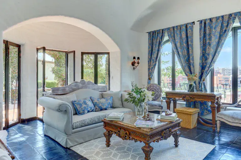 Casa Mi Besito, living room with a blue silk sofa, a carved wood coffee table, blue drapes and arched windows, San Miguel de Allende
