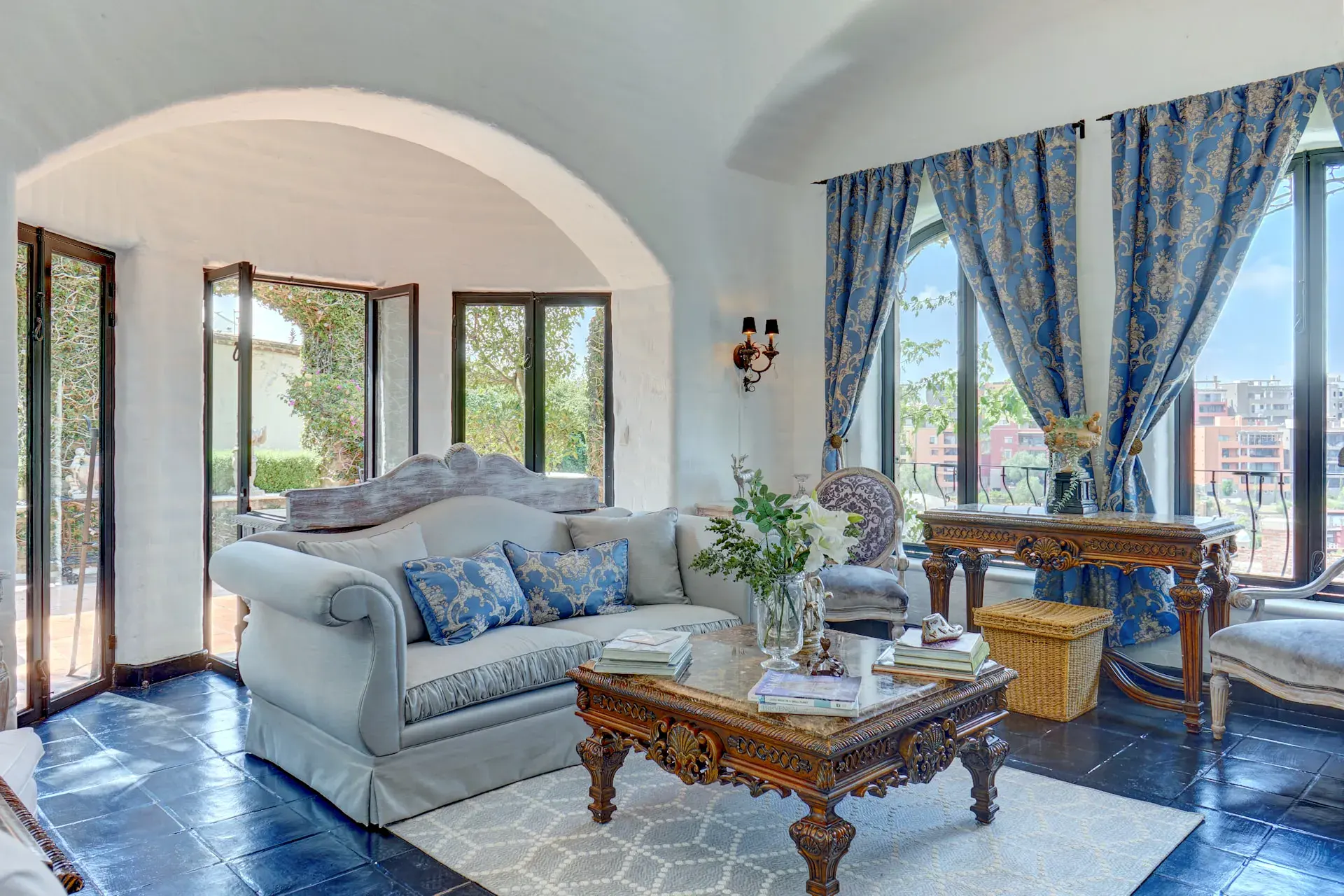 Casa Mi Besito, living room with a blue silk sofa, a carved wood coffee table, blue drapes and arched windows, San Miguel de Allende