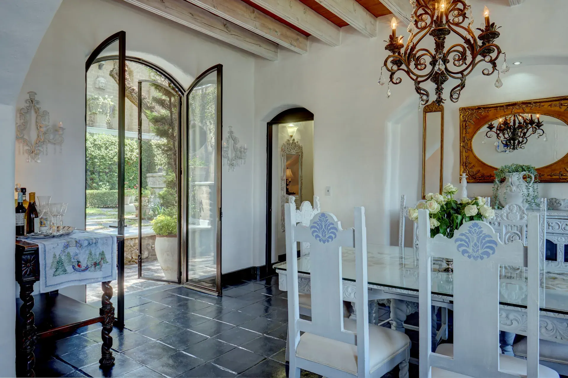 Casa Mi Besito, dining room with a glass-top table, white carved chairs, an iron chandelier and arched glass doors, San Miguel de Allende