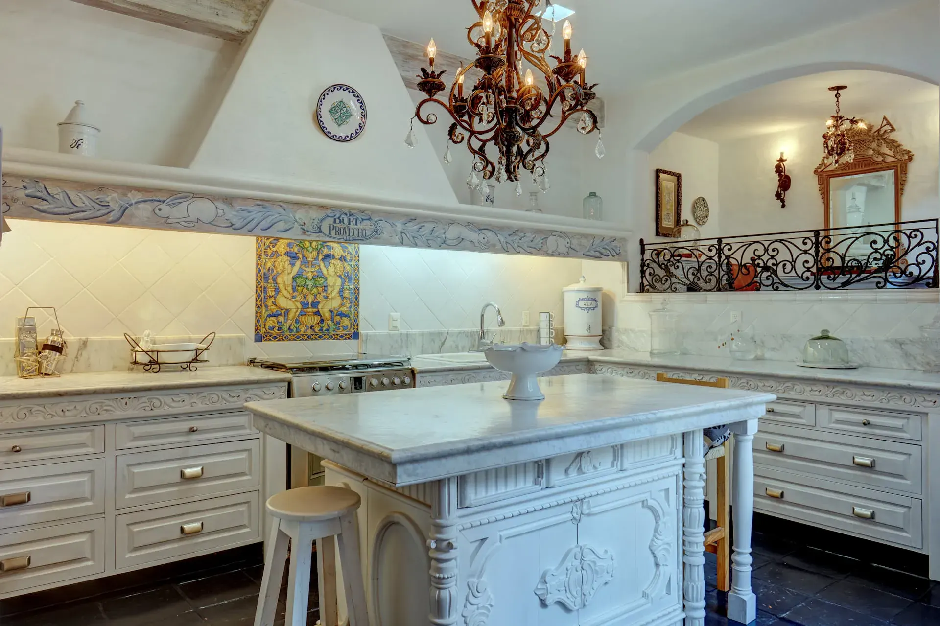 Casa Mi Besito, kitchen with a carved white island, marble counters, a decorated hood and a balcony railing above, San Miguel de Allende