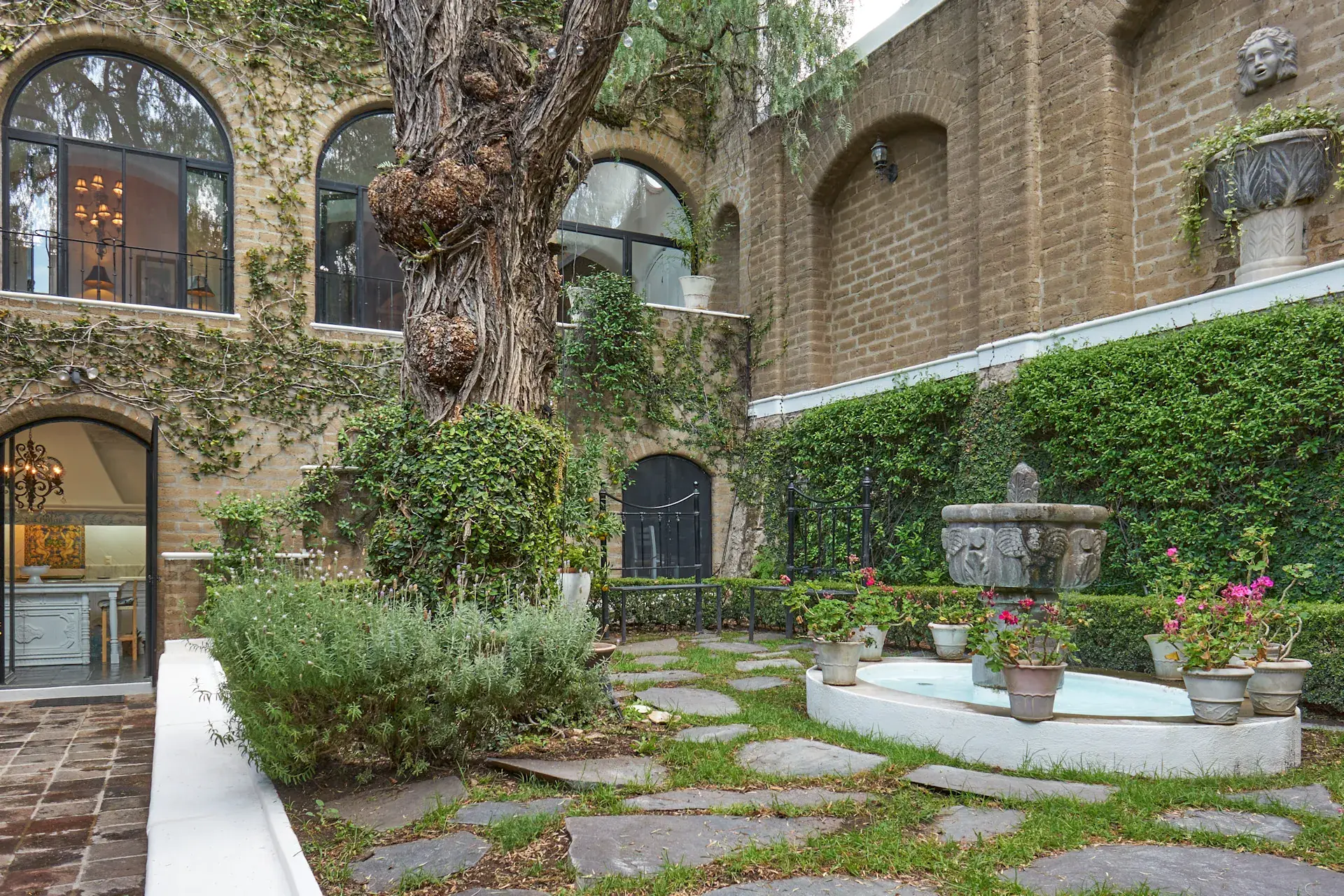 Casa Mi Besito, courtyard fountain with flagstone paving, hedges and arched windows of the house, San Miguel de Allende