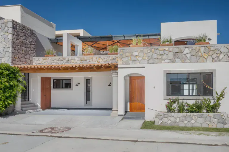 Casa Milagros, white and stone single-story house with a wood front door, a rooftop terrace with a pergola and a stone planter, San Miguel de Allende