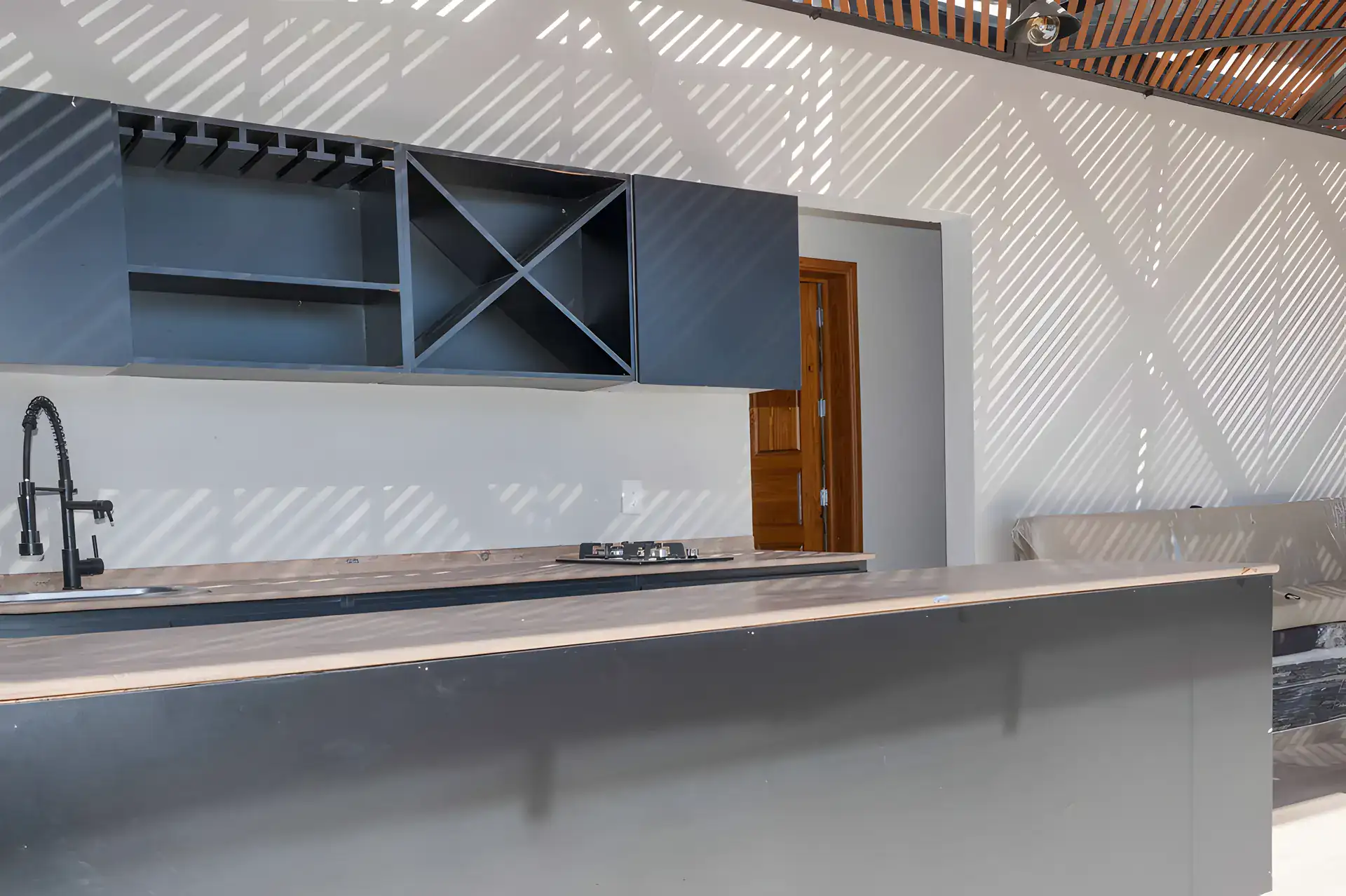 Casa Milagros, outdoor kitchen counter with a built-in cooktop, a faucet, a dark wine shelf and a patterned pergola shadow wall, San Miguel de Allende