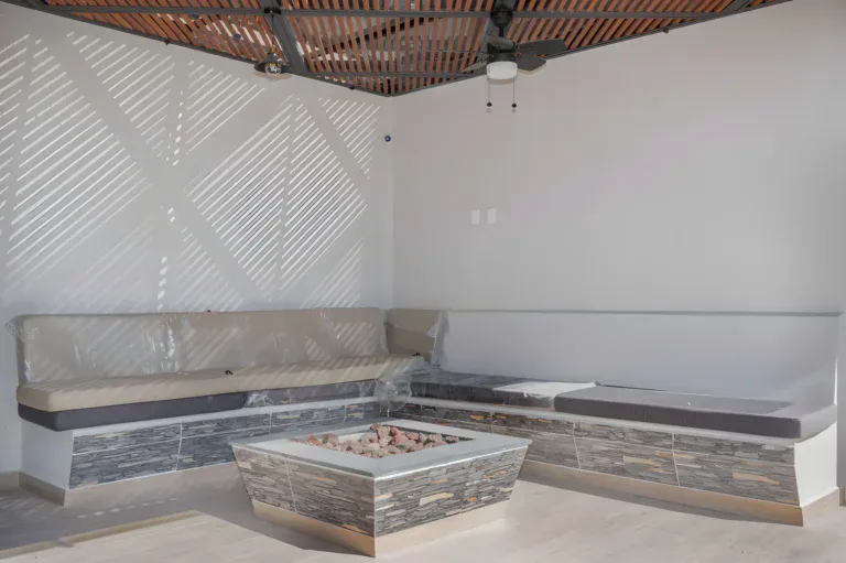 Casa Milagros, covered outdoor lounge with a built-in corner bench, a stone fire table and a ceiling fan, San Miguel de Allende