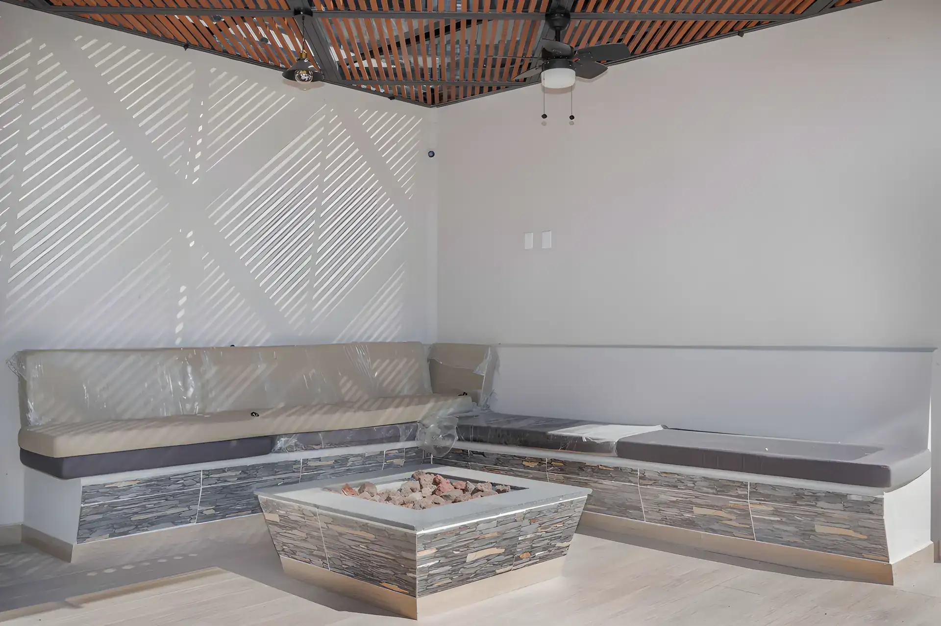 Casa Milagros, covered outdoor lounge with a built-in corner bench, a stone fire table and a ceiling fan, San Miguel de Allende