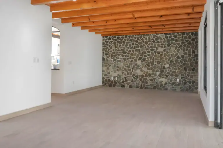 Casa Milagros, empty living room with a rough stone feature wall, a wood beam ceiling and a pale wood floor, San Miguel de Allende