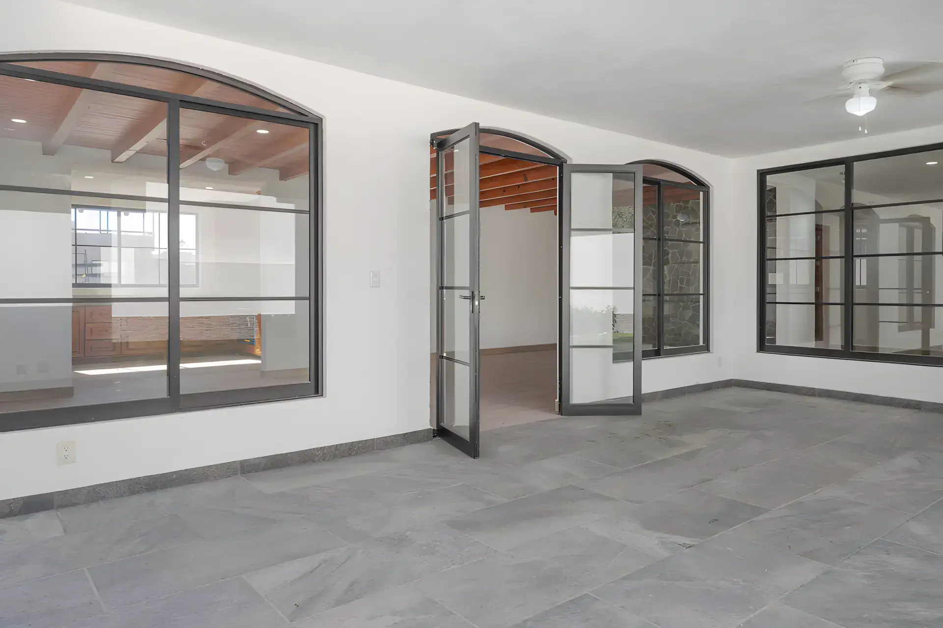 Casa Milagros, empty living room with arched steel-framed glass walls and glass doors to the patio, San Miguel de Allende