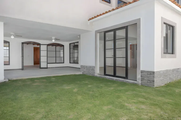 Casa Milagros, covered patio and lawn with steel-framed glass doors and a stone-clad wall base, San Miguel de Allende