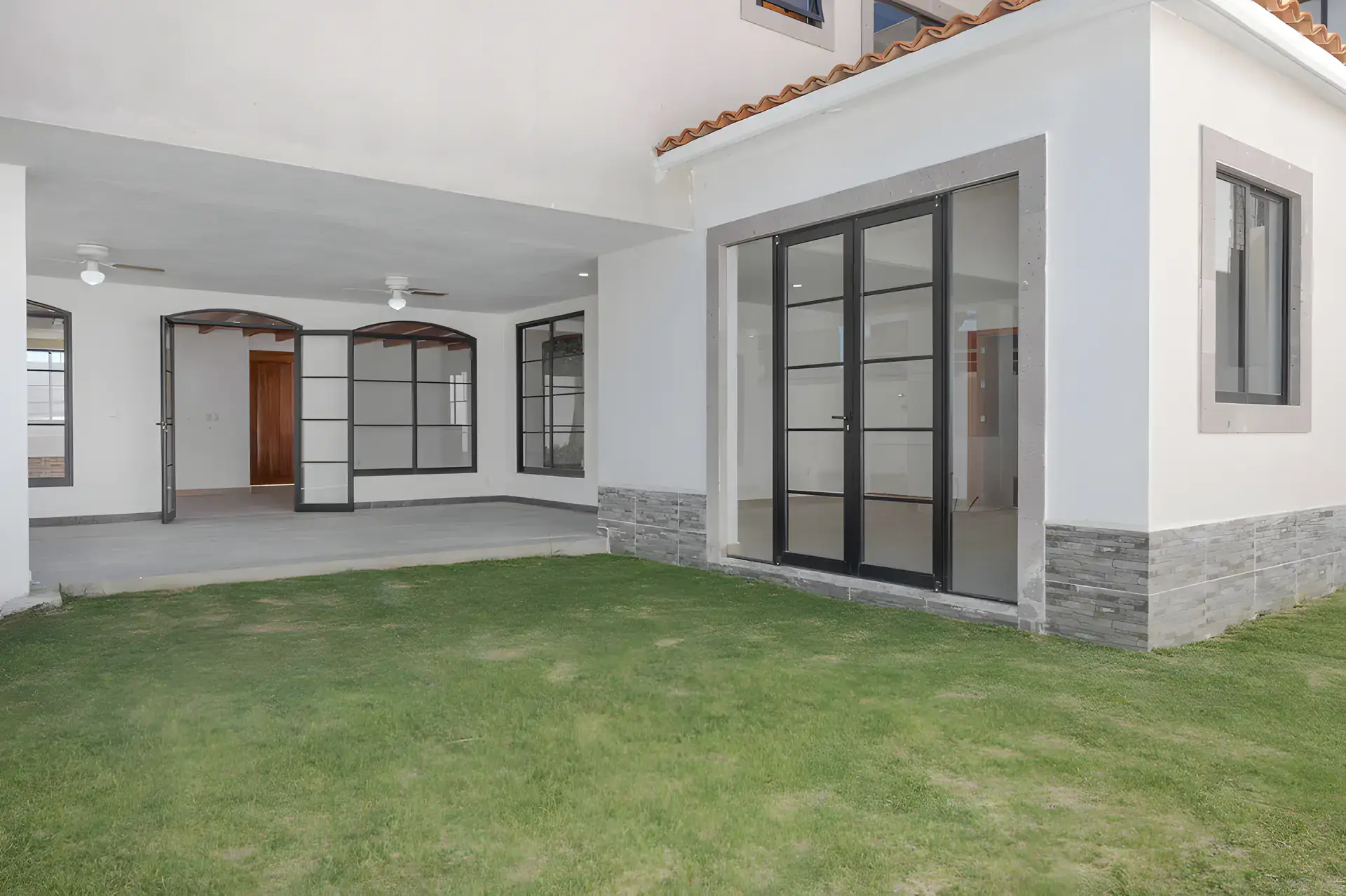 Casa Milagros, covered patio and lawn with steel-framed glass doors and a stone-clad wall base, San Miguel de Allende