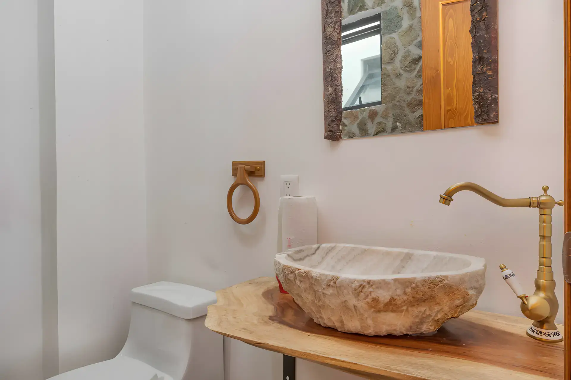 Casa Milagros, powder room with a stone vessel sink on a live-edge wood counter, a stone and wood framed mirror and a toilet, San Miguel de Allende