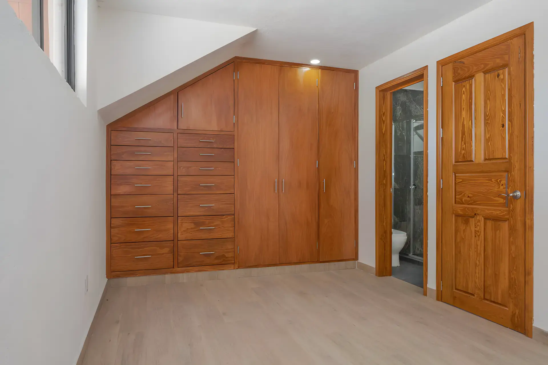 Casa Milagros, empty bedroom with a built-in wood wardrobe and drawers under the stairs and a wood door, San Miguel de Allende
