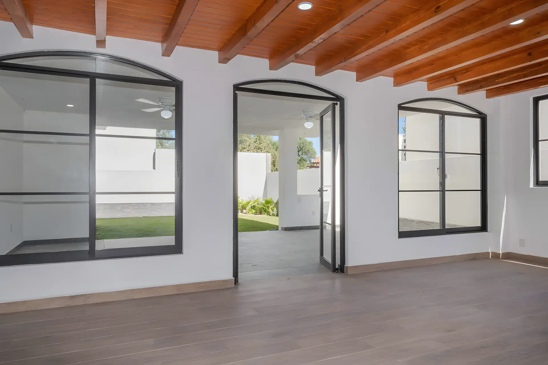 Casa Milagros, empty room with a wood beam ceiling and arched steel-framed glass doors to the covered patio, San Miguel de Allende