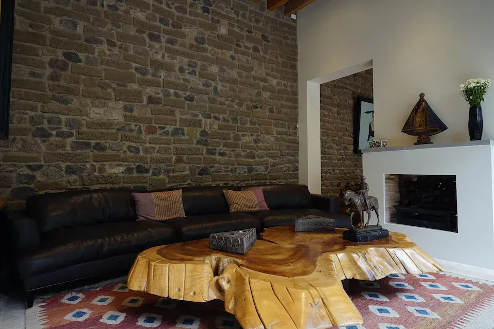 Casa Mojica, living room with an exposed brick wall, a black leather sectional and a tree-slab coffee table, San Miguel de Allende