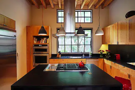 Casa Mojica, kitchen with wood cabinets, a black island with a cooktop and a steel hood, San Miguel de Allende
