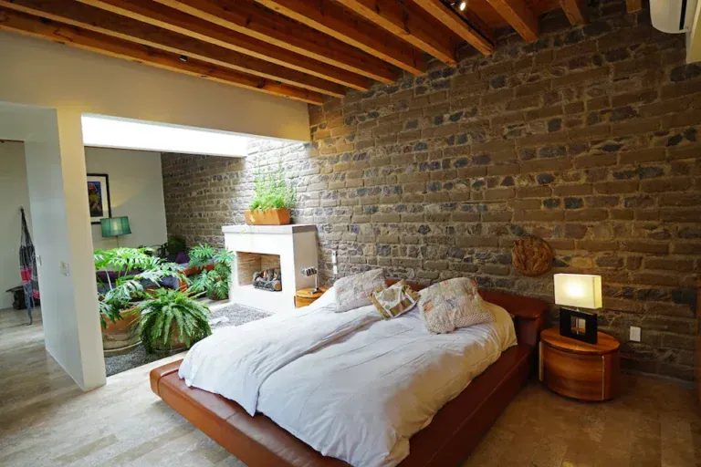 Casa Mojica, bedroom with a platform bed and a brick wall opening to a green atrium, San Miguel de Allende