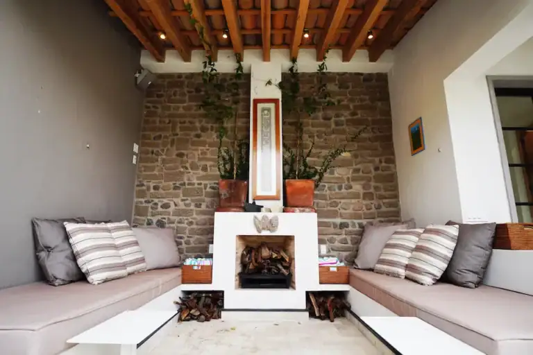 Casa Mojica, covered patio with striped sofas and a fireplace beside a brick wall, San Miguel de Allende
