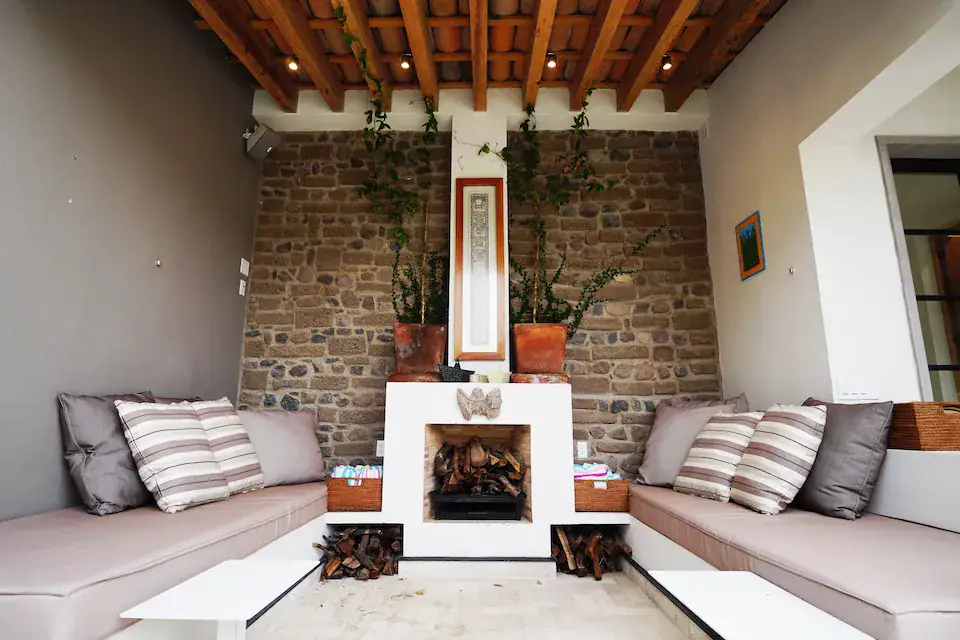 Casa Mojica, covered patio with striped sofas and a fireplace beside a brick wall, San Miguel de Allende