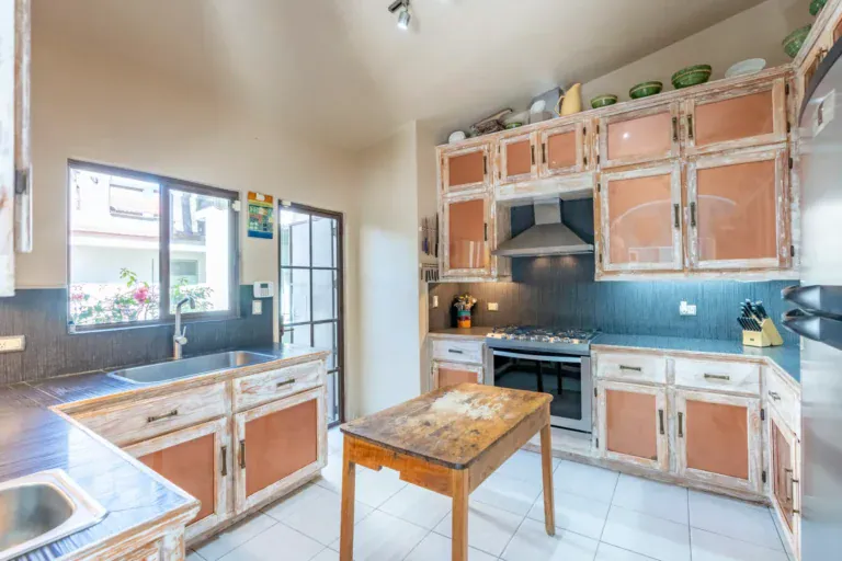 Casa Nispero, kitchen with weathered white cabinets with terracotta panels, a stainless range and a wood-top island, San Miguel de Allende