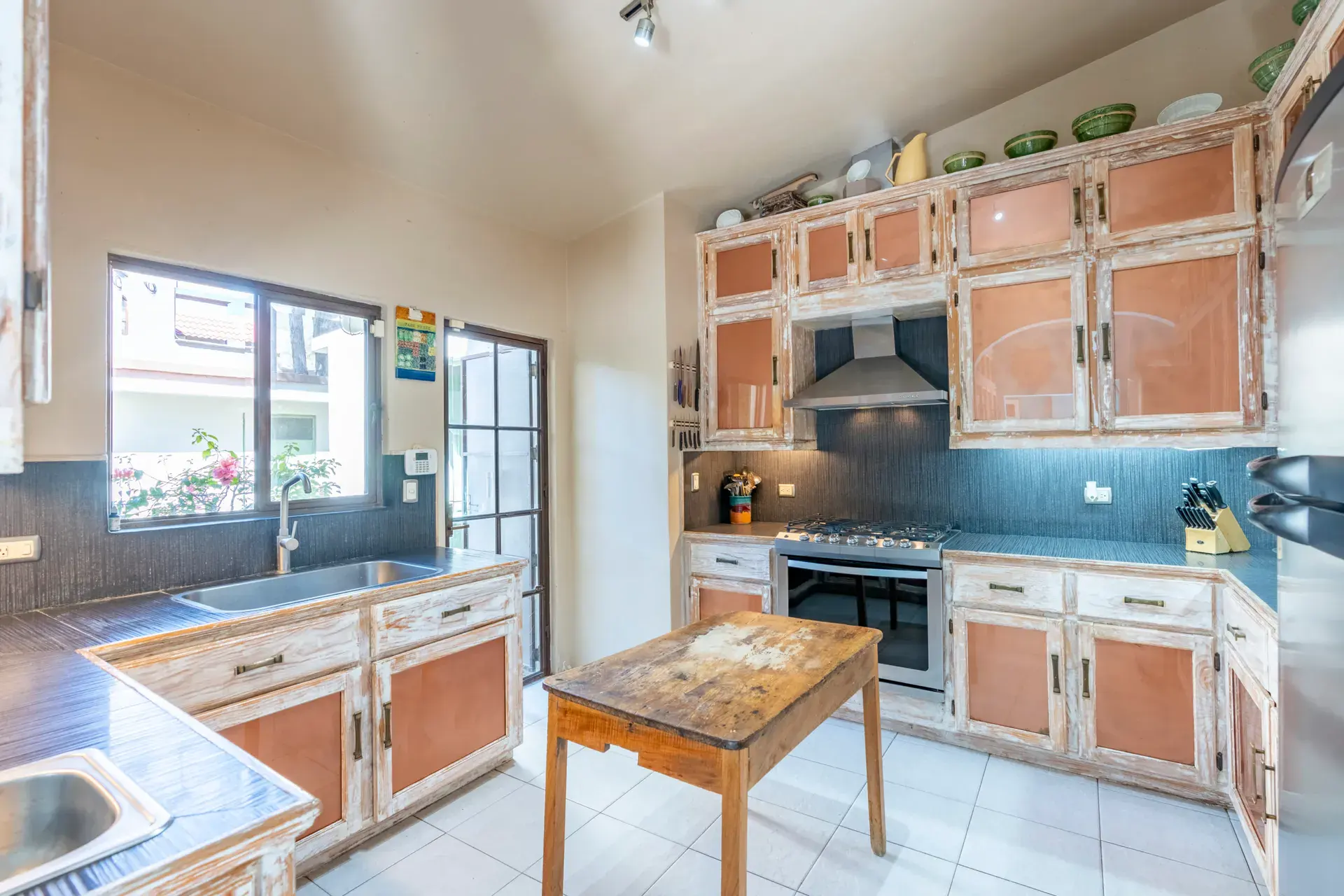 Casa Nispero, kitchen with weathered white cabinets with terracotta panels, a stainless range and a wood-top island, San Miguel de Allende